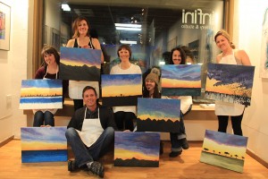Kris Dill poses with the participants of Thursday’s art class, each featuring their own unique painting. Photo by Ben Olson.