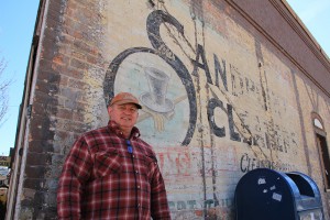Owner John Ford stands in front of the historic “ghost sign” for Sandpoint Cleaners, which operated from 1945-1960. Photo by Ben Olson.