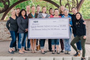 Members of 101 Women and Bonner Partners in Care stand with the “big check.” From left to right: Judy Thompson, Maureen Hammond, Jacinda Bokowy, Kelli West, Gina Woodruff, Emma Gibson, Nicole Grimm, Tracey Gibson, Amy Topp, Nancy Dooley, Becca Orchard, Angie Dail, Jennifer Macdonald. Photo by Angie Dail.