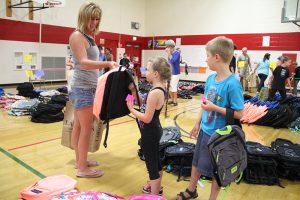 A mother and her two children pick out new backpacks at Farmin-Stidwell Elementary School on Tuesday. Photo by Ben Olson.