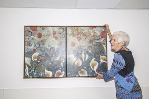 Polly Mire adjusting a painting called “Tranquility” by Catherine Earle at Bonner General Health. Photo by Cameron Barnes.