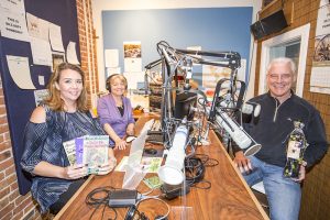 From Left to Right: Jennifer Berkey (Auction Organizer), Suzy Perez (Station Manager) and Charlie Parrish (President of the Board) hold up a few of the tangible items up for auction in the KRFY 88.5 Panhandle Community Radio Station on First Avenue. Photo by Cameron Barnes