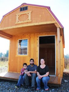 Lenny Guerrero, center, sits with his son Ezra, left, and business partner Dani Parsons, right, on the porch of a portable building that will be very similar to the cabins proposed for Hearts to Homes. Photo by Ben Olson.