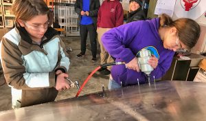 Aerospace students Caleb Watson, left, and Anne Watson, right, install replacement rivets into wing of Zenith Zodiac during plane-building project in Sandpoint airport hangar.